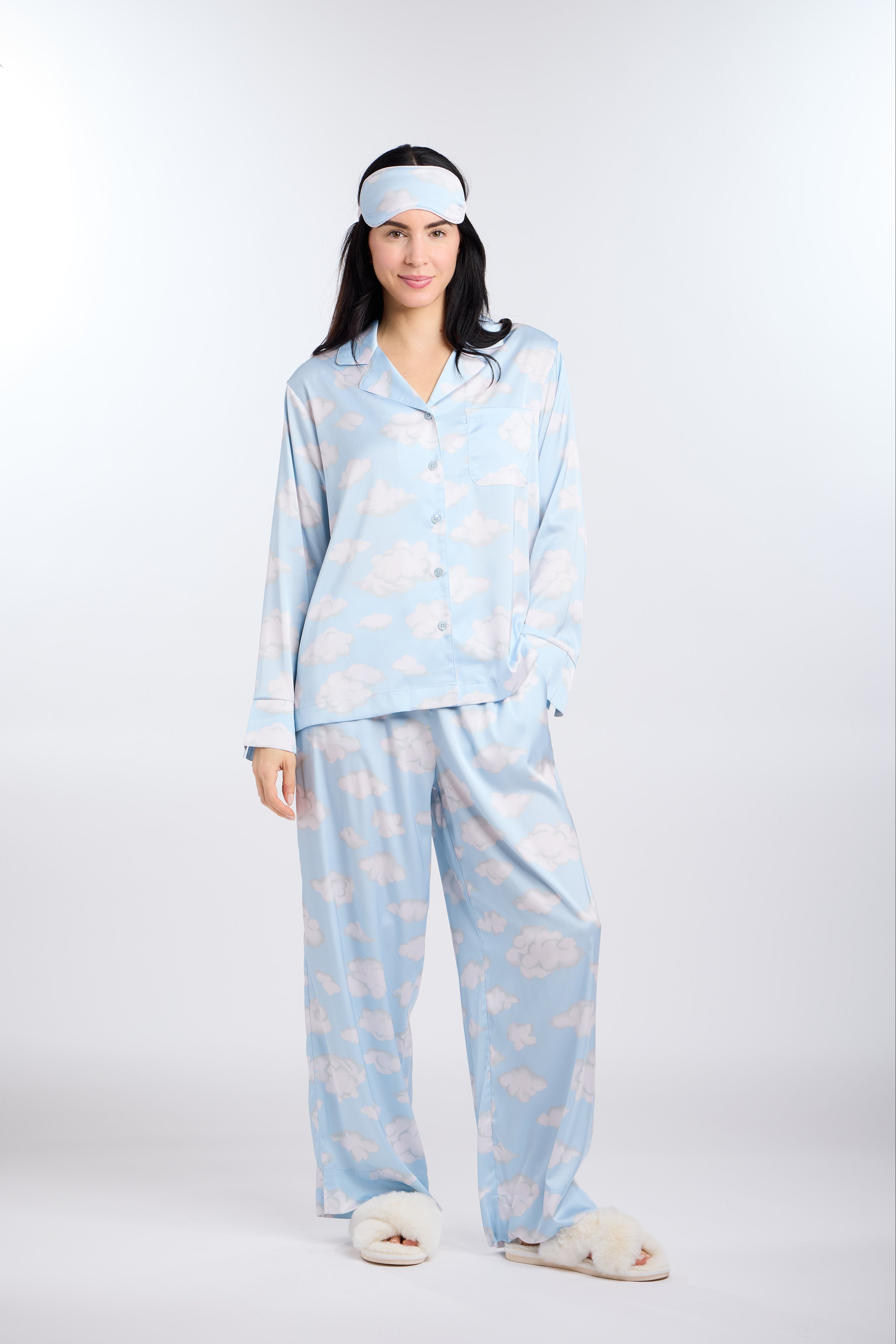 Woman wearing a light blue pajama set and eye mask with cloud pattern on a white background