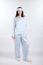 Woman wearing a light blue pajama set and eye mask with cloud pattern on a white background